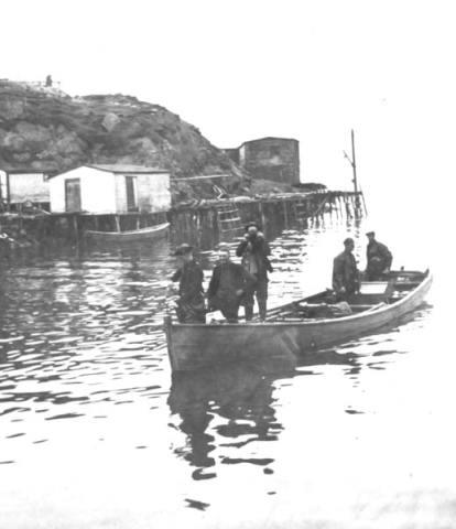 237: J V McCarthy's skiff arriving with a load of fish. J V McCarthy 2nd-left, Bill Webber  right. Leo Whalen's stage and storehouse at left, James Reddy's storehouse center.  [courtesy of Mollie McCarthy]  - J V son of Thomas McCarthy &amp;amp; Anastasia Fitzgerald; Bill son of John Webber &amp;amp; Mary Emberly
